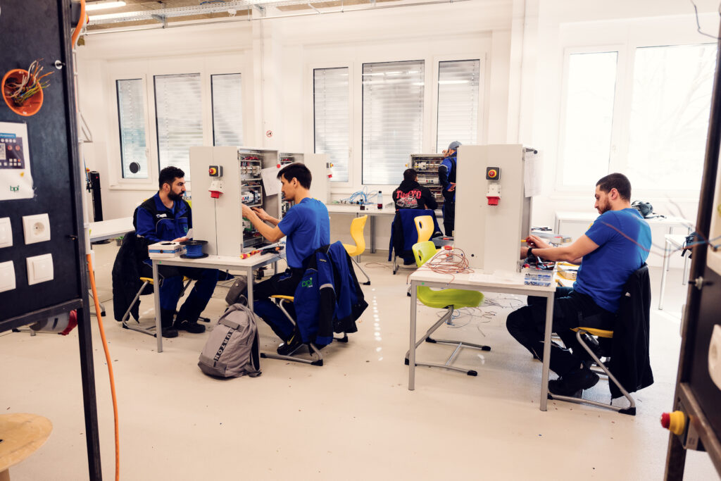 Teilnehmende verdrahten Schaltschränke an Einzeltischen in einer Schulungswerkstatt
