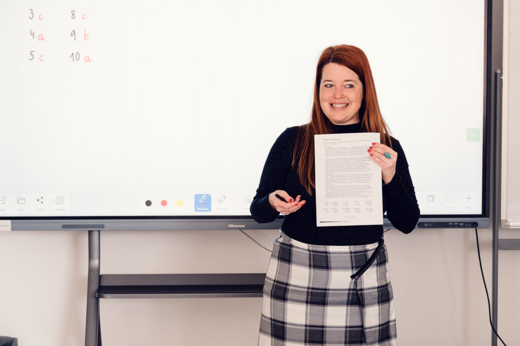 Trainerin hält vor dem Whiteboard ein ausgefülltes Formular hoch.