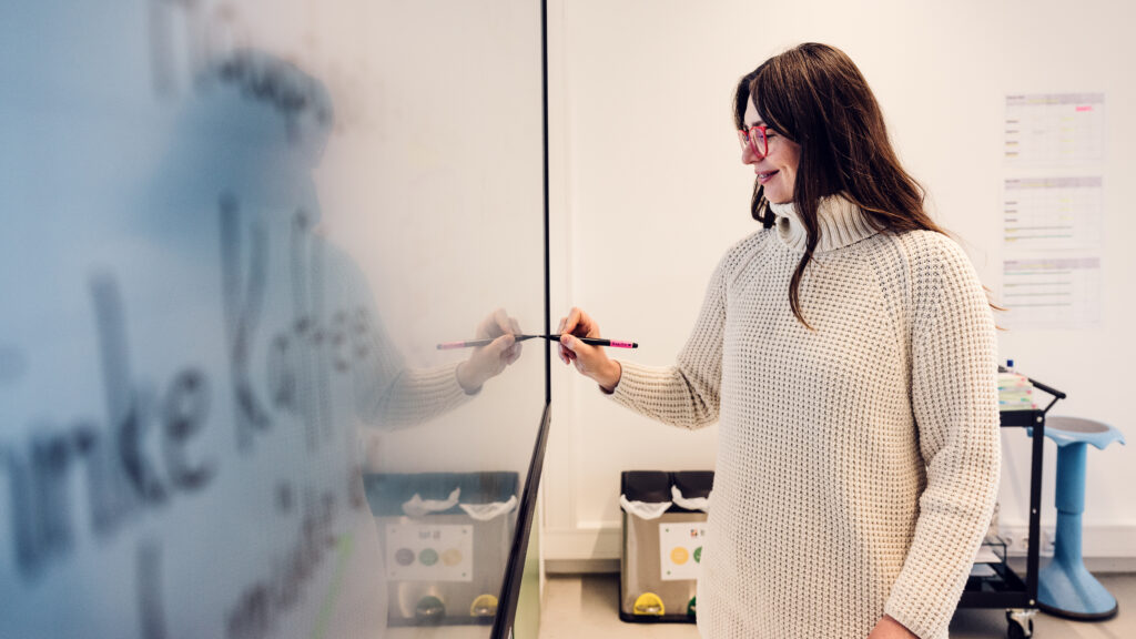 Trainerin schreibt mit einem Stift an ein Whiteboard im Schulungsraum der BPI Akademie