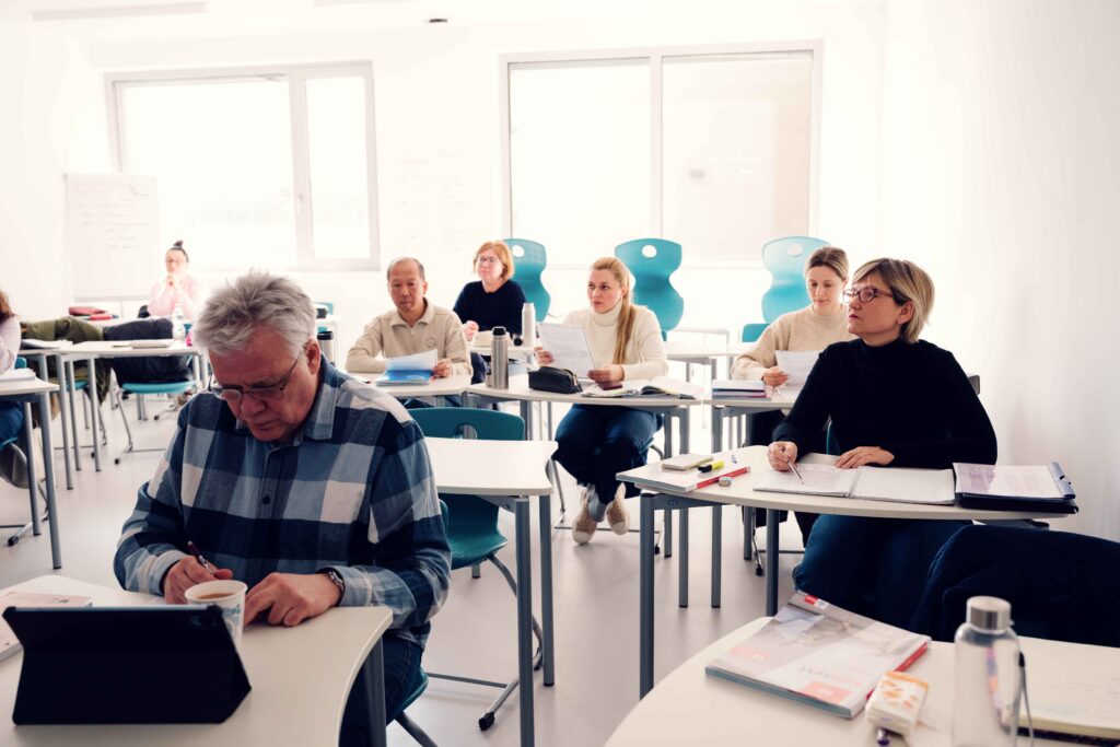 Teilnehmer:innen sitzen im Schulungsraum an Tischen und folgen dem Unterricht.