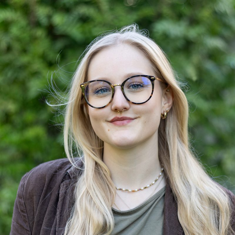 Porträt von Anne Schaller, verantwortlich für Marketing und Kommunikation der BPI Akademie, vor einer begrünten Wand